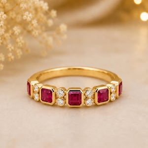 May include: A gold band ring featuring a repeating pattern of square-cut red rubies and small round white diamonds. The gemstones are set in a bezel style along the centre of the polished yellow gold band, creating a continuous decorative design.
