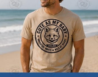 Pode incluir: Uma t-shirt bege de manga curta com um gráfico circular preto no peito. O design inclui uma ilustração de uma raposa, o texto CUTE AS MY BABY, ADVENTURE AWAITS, WILD AT HEART, SINCE 2026 e um pequeno ícone de pegada de pata.