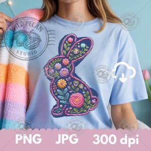 May include: Light blue t-shirt featuring a detailed floral bunny design in shades of pink, yellow, and green. The design is embroidered with a dark blue outline. The shirt has the text "WILD PECAN STUDIO" and "PNG JPG 300 dpi".