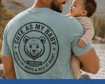 Pode incluir: Uma camiseta azul clara com um desenho circular de um rosto de urso e o texto "CUTE AS MY BABY". Uma pessoa segura um bebê. A camisa também tem o texto "ADVENTURE AWAITS WILD AT HEART SINCE 2026". A parte inferior da imagem mostra "DIGITAL ONLY SVG PNG JPG".