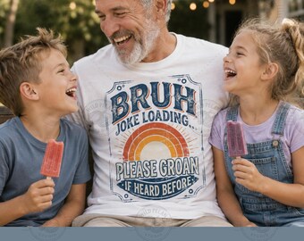 Pode incluir: Uma camiseta branca com o texto "BRUH JOKE LOADING... PLEASE GROAN IF HEARD BEFORE" em um design retrô. A imagem mostra um homem e duas crianças rindo enquanto seguram picolés. O fundo está desfocado com vegetação.