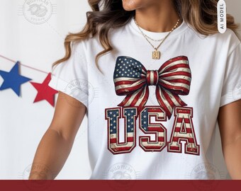 Pode incluir: Uma t-shirt branca de manga curta com um gráfico grande de um laço com o padrão da bandeira americana acima das letras USA, que também estão preenchidas com um design de estrelas e riscas vermelhas, brancas e azuis. O gráfico tem textura.