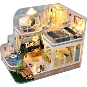 Puede incluir: Casa de muñecas en miniatura de varios niveles, con piano, sala de estar, dormitorio y comedor. La casa de muñecas tiene una combinación de colores azul y blanco, con una piscina y un telón de fondo oceánico. El interior está iluminado con pequeñas luces.