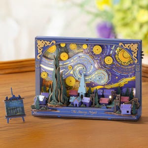 May include: A blue wooden diorama depicting Van Gogh's "The Starry Night" with a miniature easel and painting. The scene includes a village, swirling sky, and illuminated stars. The text "The Starry Night" is visible.