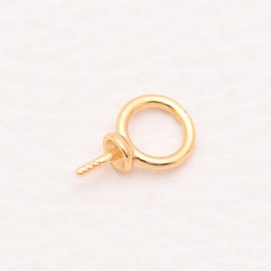 May include: A gold-toned metal screw eye bail featuring a circular loop at the top and a threaded post at the bottom. This jewelry component is designed for attaching pendants or charms to necklaces or bracelets, showcasing a smooth finish.
