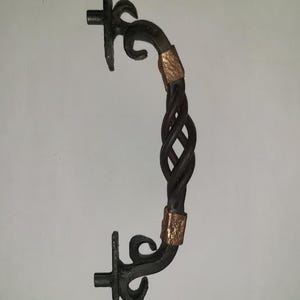 May include: A wrought iron door handle with a twisted center and decorative ends. The handle is dark gray with copper-colored accents. The overall design is ornate and rustic, suitable for a vintage or farmhouse aesthetic.