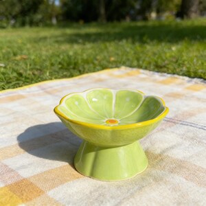 Peut inclure: Un bol en c&eacute;ramique en forme de tranche de citron vert avec un int&eacute;rieur vert clair, des segments blancs et un bord jaune. Le bol repose sur une base en pi&eacute;destal &eacute;vas&eacute;e et pr&eacute;sente une surface ext&eacute;rieure textur&eacute;e imitant l'&eacute;corce.