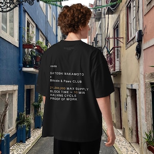Könnte beinhalten: Schwarzes T-Shirt mit weißem Text auf der Rückseite, darunter "code", "SATOSHI NAKAMOTO" und "Bitcoin & Paws CLUB". Der Text listet auch "21.000.000 MAX SUPPLY" und weitere Details auf. Das T-Shirt wird von einer Person im Freien getragen.