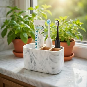 May include: A marble-effect toothbrush holder with bamboo dividers, containing a tube of toothpaste and two electric toothbrushes. The toothbrushes are white and black, with blue and white bristles. The toothpaste tube has green leaf graphics.