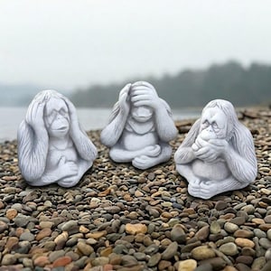 May include: Three light gray stone-colored statues of orangutans in a seated position. The first orangutan covers its ears, the second covers its eyes, and the third covers its mouth, each with detailed fur textures and realistic facial features.