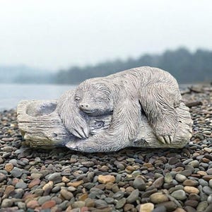 May include: A gray, textured sloth figurine resting on a hollowed-out log. The sloth has detailed fur carvings, closed eyes, and long claws, with a small open cavity on the left side of the log structure, designed as a planter or decorative container.