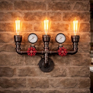 Puede incluir: Aplique de pared de estilo industrial con tres bombillas Edison. La lámpara está hecha de tuberías de metal oscuro, con válvulas rojas y manómetros. El aplique está montado en una pared de ladrillo, creando una estética vintage.