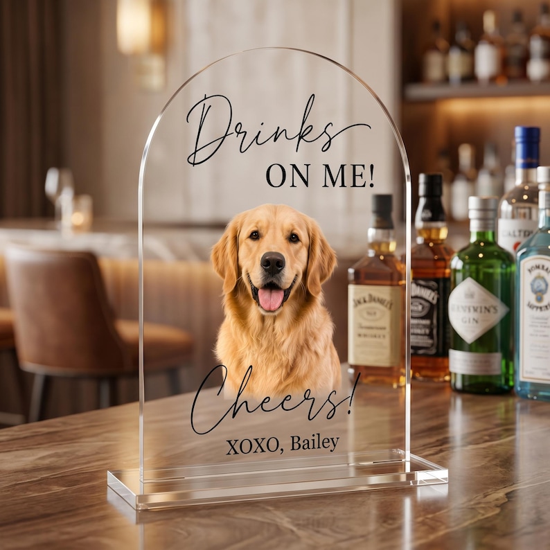 Personalized acrylic pet wedding bar sign featuring a golden retriever portrait with “Drinks On Me” wording, elegant script text, and custom pet name detail. This custom dog signature drink sign is perfect for wedding bar decor, cocktail hour, reception table styling, bridal shower, engagement party, or pet-themed celebration. Available in clear, white, frosted, and black acrylic, it adds a charming and playful touch to your event setup.