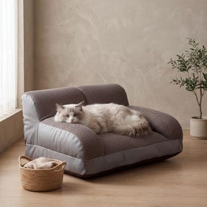 Puede incluir: Un sofá gris y marrón para mascotas con un gato durmiendo. El sofá tiene una tela de malla y un borde gris. Una pequeña cesta tejida se encuentra frente al sofá. Una pequeña planta en maceta está en el fondo.