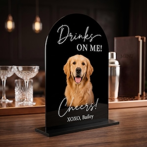Personalized acrylic pet wedding bar sign featuring a golden retriever portrait with “Drinks On Me” wording, elegant script text, and custom pet name detail. This custom dog signature drink sign is perfect for wedding bar decor, cocktail hour, reception table styling, bridal shower, engagement party, or pet-themed celebration. Available in clear, white, frosted, and black acrylic, it adds a charming and playful touch to your event setup.