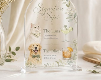 Op de afbeelding: Transparant acryl bruiloftbord met een gewelfde bovenkant, met de tekst "Signature Sips". Het bevat illustraties van een kat en een hond, samen met cocktailnamen en ingrediënten: The Luna en The Oliver.