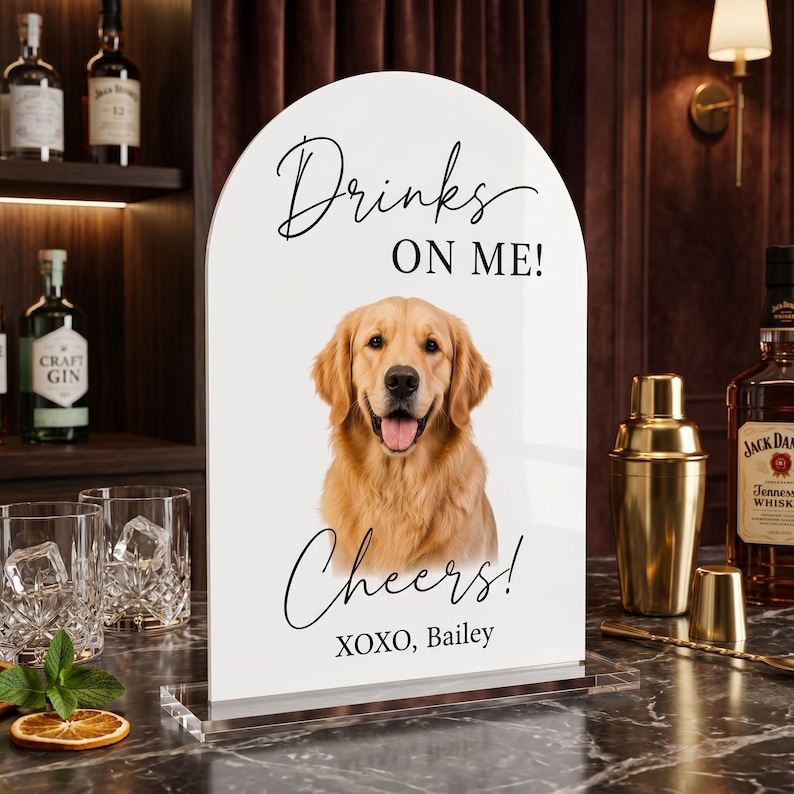 Personalized acrylic pet wedding bar sign featuring a golden retriever portrait with “Drinks On Me” wording, elegant script text, and custom pet name detail. This custom dog signature drink sign is perfect for wedding bar decor, cocktail hour, reception table styling, bridal shower, engagement party, or pet-themed celebration. Available in clear, white, frosted, and black acrylic, it adds a charming and playful touch to your event setup.