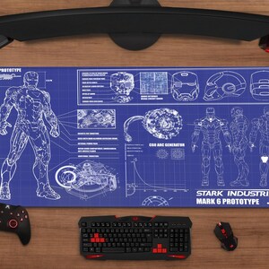 May include: A blue and white Stark Industries Mark 6 Prototype mousepad with schematics and illustrations. A black keyboard, mouse, and controller are on a wooden surface. The mousepad features the text "STARK INDUSTRIES MARK 6 PROTOTYPE".