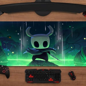 Pode incluir: Tapete de rato retangular para jogos com um personagem de Hollow Knight em um cenário verde escuro e azul. Um teclado, um rato, um controlador e um fone de ouvido circundam o tapete.