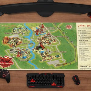 May include: A gaming setup featuring a large mousepad with a map of "Nuka-World" from Fallout 4. The map is surrounded by a black keyboard, mouse, controller, and headset. The keyboard and mouse have red accents.