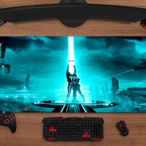 Könnte beinhalten: Rechteckiges Gaming-Mauspad mit futuristischem Sci-Fi-Design in Türkis und Schwarz. Es zeigt ein Paar unter einem hellen Licht. Tastatur, Maus, Controller und Headset sind auf einer Holzoberfläche zu sehen.