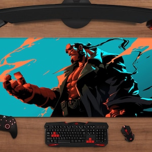 May include: A rectangular mouse mat featuring a Hellboy illustration against a teal background with orange accents. The artwork depicts Hellboy in a dynamic pose, with a black coat and red skin. A gaming setup surrounds the mat.