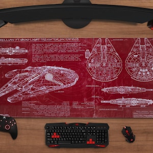 Könnte beinhalten: Rotes und weißes Mauspad mit einem Schema des Corellian YT-1300 Light Freighter (Modified). Eine schwarze Tastatur, Maus, Controller und Headset sind auf einer Holzoberfläche darum angeordnet.