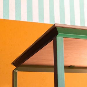 Peut inclure: Une table dotée d'un plateau en bois plat avec un bord stratifié visible, soutenue par un cadre en métal vert. La structure se compose de pieds verticaux droits et de traverses horizontales fixées sous la surface du plateau.