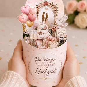 May include: A pink and gold wedding-themed pop-up card with heart-shaped balloons, a tiered cake, champagne, and a ring box. The card features a floral archway and the words "Von Herzen Alles Liebe zur Hochzeit."