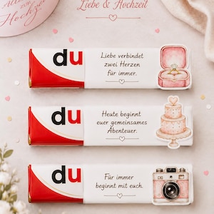 May include: A wedding-themed image featuring three chocolate bars with the word "du" in red and white packaging. Each bar has a different message and illustration: a ring, a cake, and a camera. The text "Liebe & Hochzeit" is also visible.