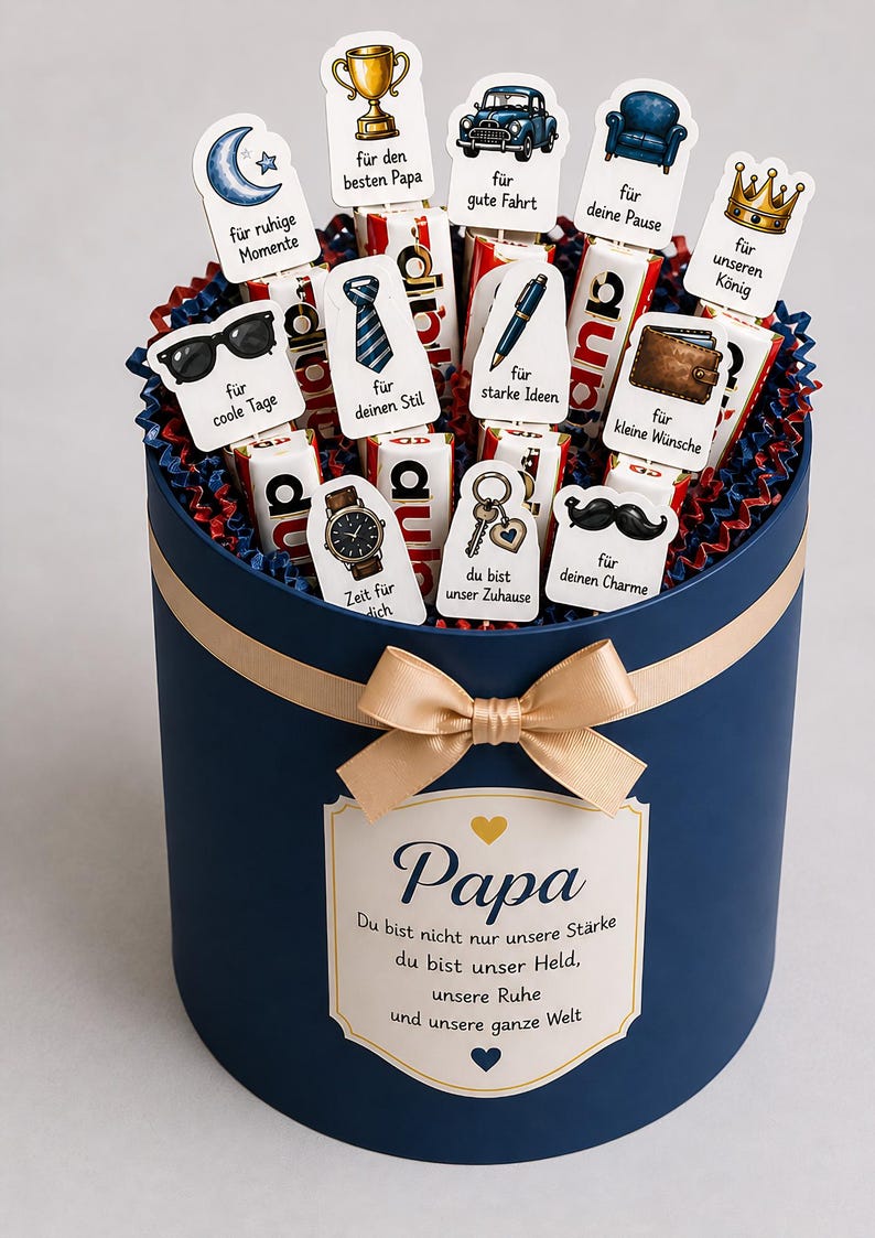 May include: A navy blue gift box with a gold ribbon and bow, filled with chocolate bars and decorative toppers. The toppers feature various illustrations and phrases, including a trophy, car, and the word "Papa".