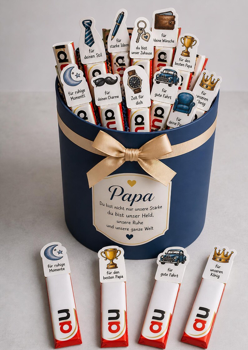 May include: A navy blue gift box with a gold bow, filled with chocolate bars and decorative toppers. The toppers feature various designs and phrases, including a tie, mustache, and car. The box has a label that says "Papa".