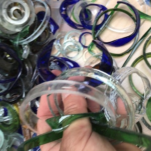 May include: A close-up of a pile of colorful glass bottle rings. The rings are in various shades of blue, green, and clear. Some of the rings are stacked on top of each other, while others are scattered around.