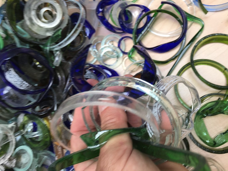 May include: A close-up of a pile of colorful glass bottle rings. The rings are in various shades of blue, green, and clear. Some of the rings are stacked on top of each other, while others are scattered around.