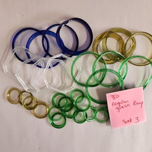 May include: A collection of glass rings in various colors, including blue, green, and gold. Some rings are clear and hexagonal. A pink sticky note reads "3D Regular glass Rays Set 3."