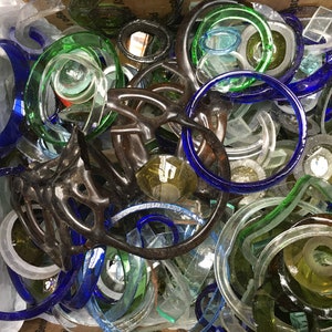 May include: A collection of glass bottle tops in various colors, including blue, green, and clear. The tops are arranged in a random pattern and some are stacked on top of each other.