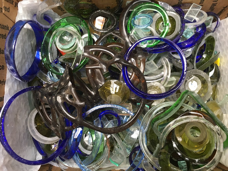 May include: A collection of glass bottle tops in various colors, including blue, green, and clear. The tops are arranged in a random pattern and some are stacked on top of each other.