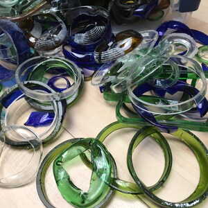 May include: A pile of glass bottle rings in various shades of blue, green, and clear. The rings are arranged in a random pattern on a wooden surface.