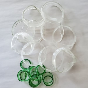 May include: A collection of clear glass rings, some larger and some smaller, with a pile of smaller green glass rings in the center.