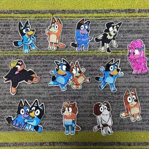 May include: A selection of embroidered patches depicting cartoon dog characters in various poses and colours. The patches feature blue, orange, black, and pink dogs with different expressions and outfits. These patches are likely for clothing or accessories.