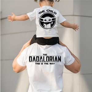 May include: White t-shirts with black graphics. One shirt reads "THE CHILD" with a circular image of a character. The other shirt says "THE DADALORIAN" and "THIS IS THE WAY".