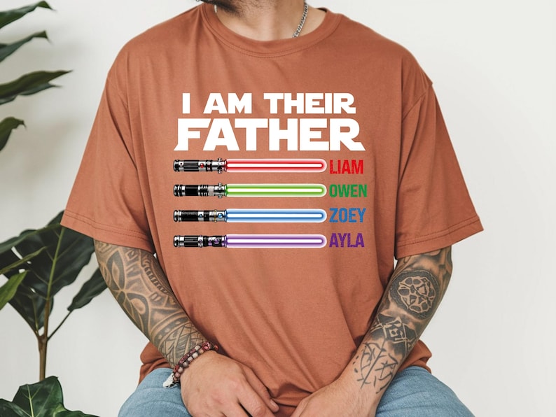 May include: A rust-colored t-shirt with the text "I AM THEIR FATHER" in white. Below the text are four lightsabers with the names Liam, Owen, Zoey, and Ayla. The lightsabers have red, green, blue, and purple blades.