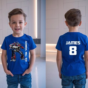 May include: A blue t-shirt featuring a graphic of a robot with the text "AUTOBOTS, ROLL OUT!" on the front. The back of the shirt displays the name "JAMES" and the number "8" in white.
