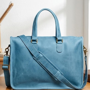 May include: A blue leather briefcase with a top handle and a detachable shoulder strap. The bag features brass-colored hardware and a rectangular shape. The leather has a slightly distressed appearance.