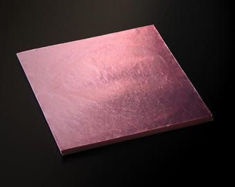 May include: A square sheet of rose gold leafing, with a textured surface, is displayed against a black background. The metallic sheet has a subtle sheen, reflecting light. This decorative material is used for crafts and artistic projects.