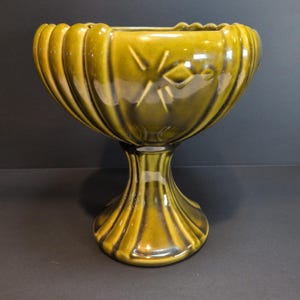 Peut inclure: Un bol sur pied en céramique vert olive brillant avec un design extérieur cannelé et festonné. Le bol présente une large ouverture évasée et une base étroite et cannelée. Un motif en étoile est gravé sur le côté du bol, ajoutant du relief.
