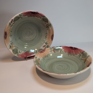 May include: Two ceramic bowls featuring a pale green interior with a visible swirl pattern. The wide rims are decorated with a painted floral motif in shades of pink, peach, and green. One bowl is positioned upright, while the other rests flat.