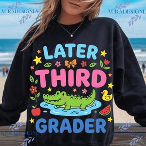 Könnte beinhalten: Schwarzes Sweatshirt mit den Worten "LATER THIRD GRADER" in Blau, Pink und Grün. Das Design umfasst einen Cartoon-Alligator, Sterne, Blumen und eine Wassermelonenscheibe. Ein lustiges, farbenfrohes Design für einen Schüler.