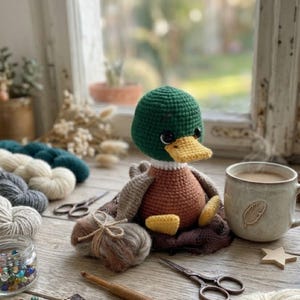Puede incluir: Un mu&ntilde;eco de pato de ganchillo hecho a mano con cabeza verde, cuerpo naranja y pico amarillo. El pato est&aacute; sobre una superficie de madera con hilo, tijeras y una taza de caf&eacute;. Un art&iacute;culo encantador y artesanal.