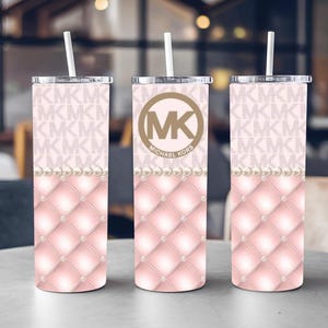 Könnte beinhalten: Drei Edelstahlbecher mit Deckeln und Strohhalmen. Die Becher haben ein rosa Steppmuster, ein Perlenband und das Michael Kors Logo. Der Hintergrund ist verschwommen.